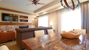 A spacious living area with a wooden dining table, a sofa, and a television mounted on the wall.