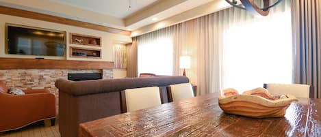 A spacious living area with a wooden dining table, a sofa, and a television mounted on the wall.
