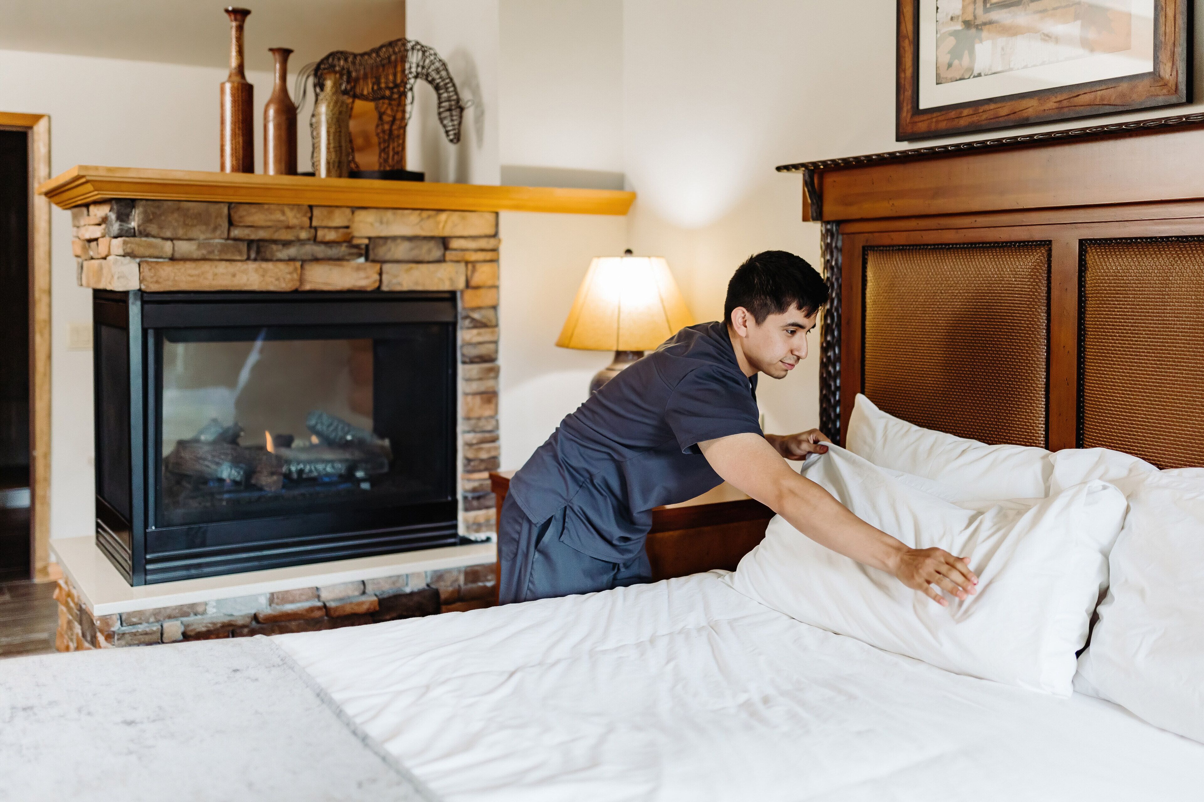 A hotel room with a stone fireplace, a bed with white linens, and a wooden headboard.
