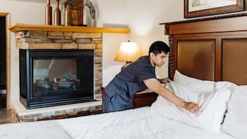 Een hotelkamer met een stenen open haard, een bed met witte lakens en een houten hoofdbord.