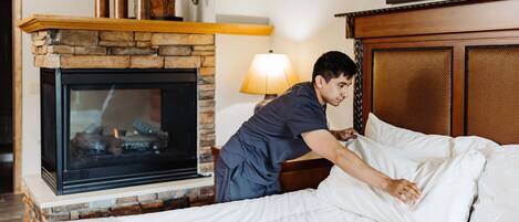 Una habitación de hotel con chimenea de piedra, cama con ropa blanca y cabecera de madera.