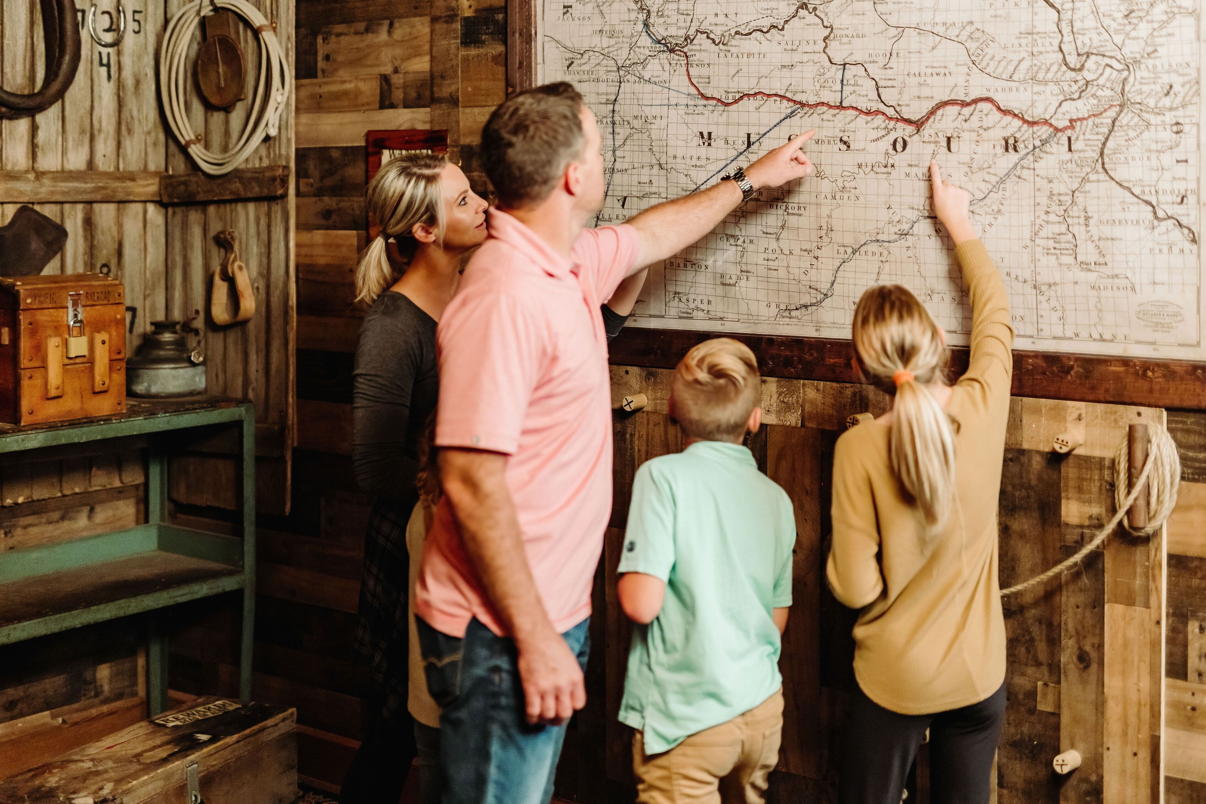 Une famille de quatre personnes examine une grande carte affichée sur un mur en bois.
