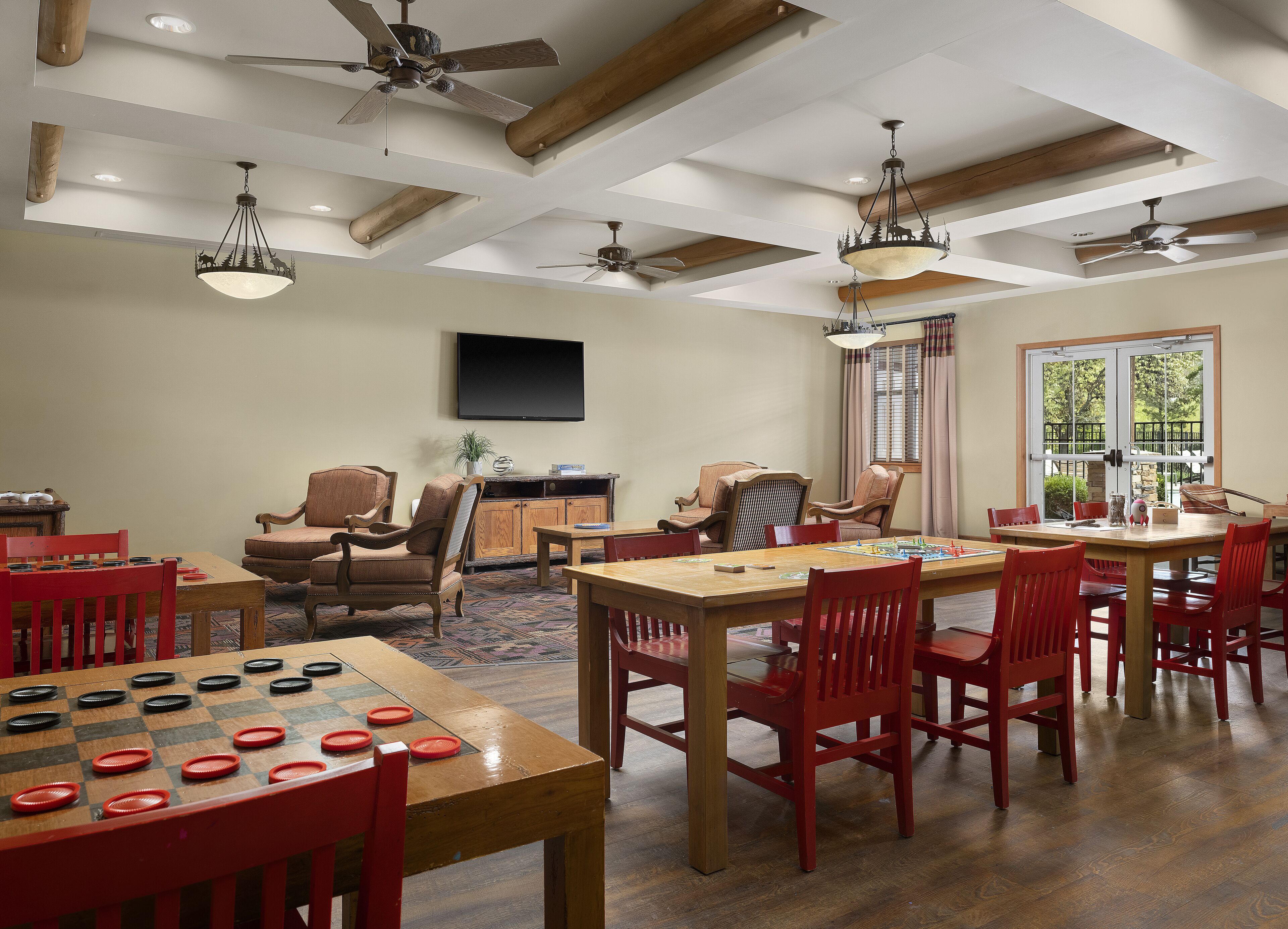A spacious room with a large wooden table, red chairs, and a ceiling fan.