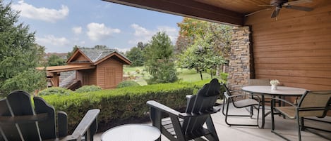 A covered patio with outdoor furniture, a ceiling fan, and a view of a house and garden.