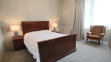 Een keurig opgemaakt slaapkamer met een groot houten bed, twee nachtkastjes met lampen, een stoel en een raam met gordijnen.