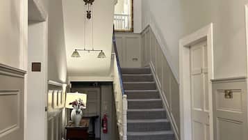 A hallway with a staircase, white walls, and a wooden floor.
