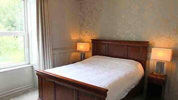 A bedroom with a large bed, two bedside tables with lamps, a chandelier, and a window with curtains.