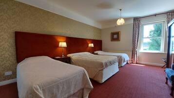 Une chambre d’hôtel avec deux lits, une tête de lit en bois, deux lampes de chevet, un radiateur, une fenêtre avec des rideaux et un tableau au mur.