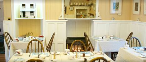 A dining area with tables set for four, chairs, and a mirror above the fireplace.