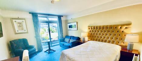 A hotel room with a large bed, a sofa, a chair, a table, and a window with curtains.