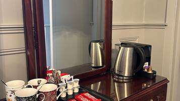 A wooden dresser with a mirror, a tray with mugs, coffee pots, and a small statue.