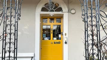 A yellow door with a white bench to the left, a brown mat at the entrance, and a wrought iron gate.