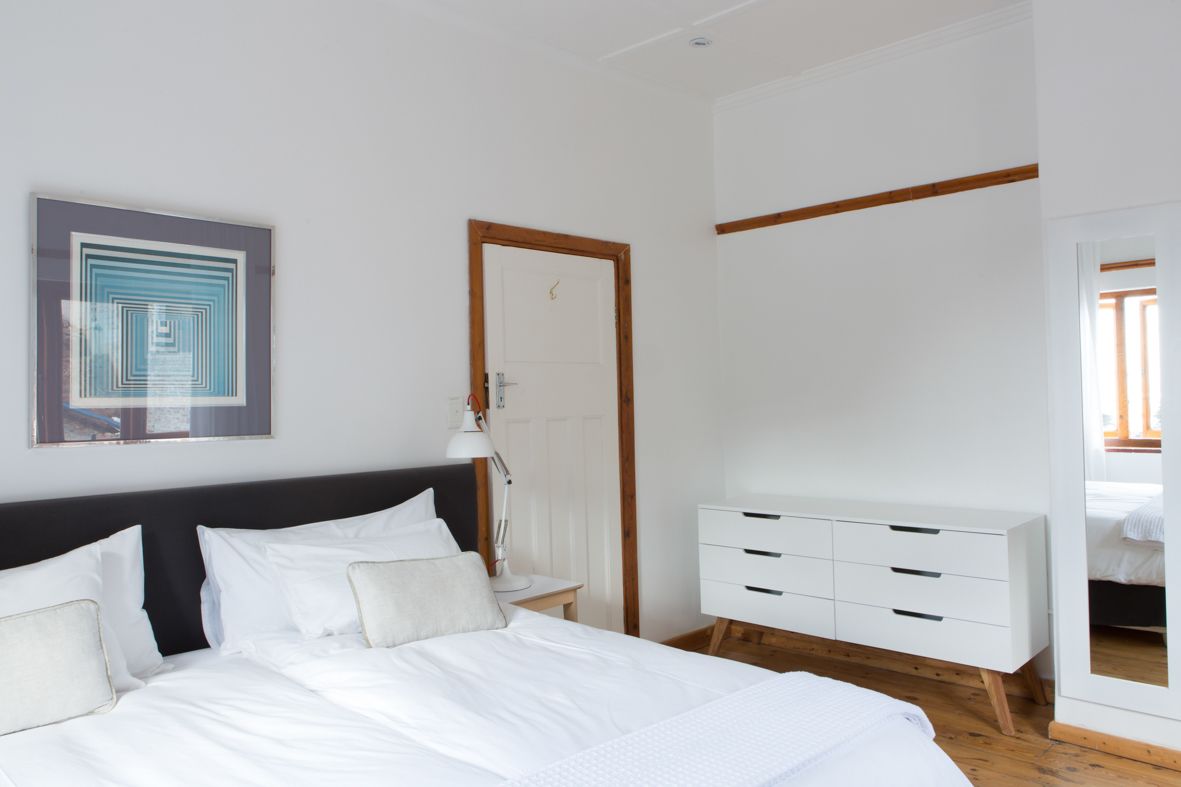 A bedroom with a large bed, a white dresser, a door, and a framed artwork on the wall.