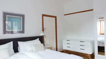 A bedroom with a large bed, a white dresser, a door, and a framed artwork on the wall.