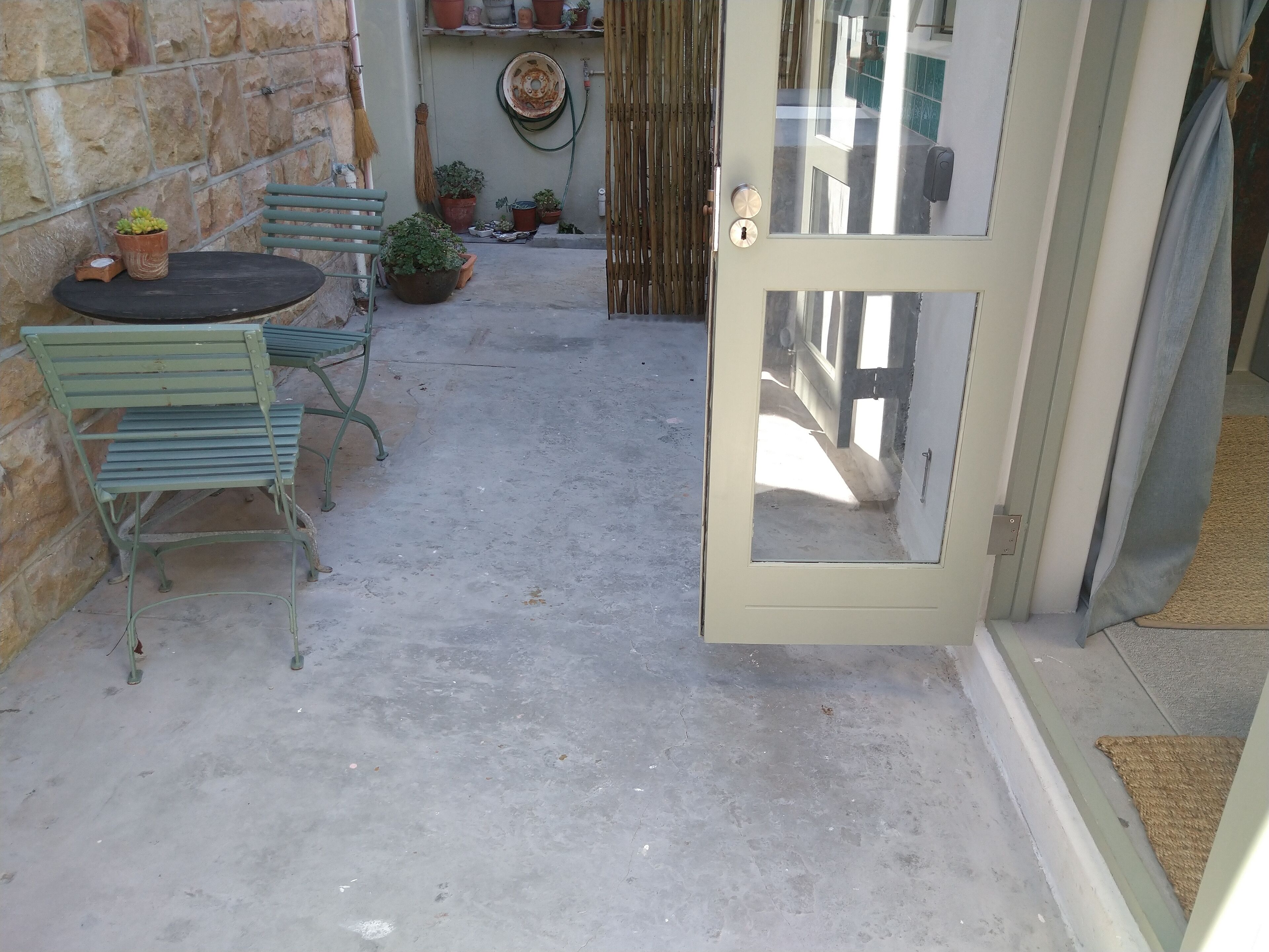 A small patio with a table and chairs, potted plants, and a door leading to the interior.