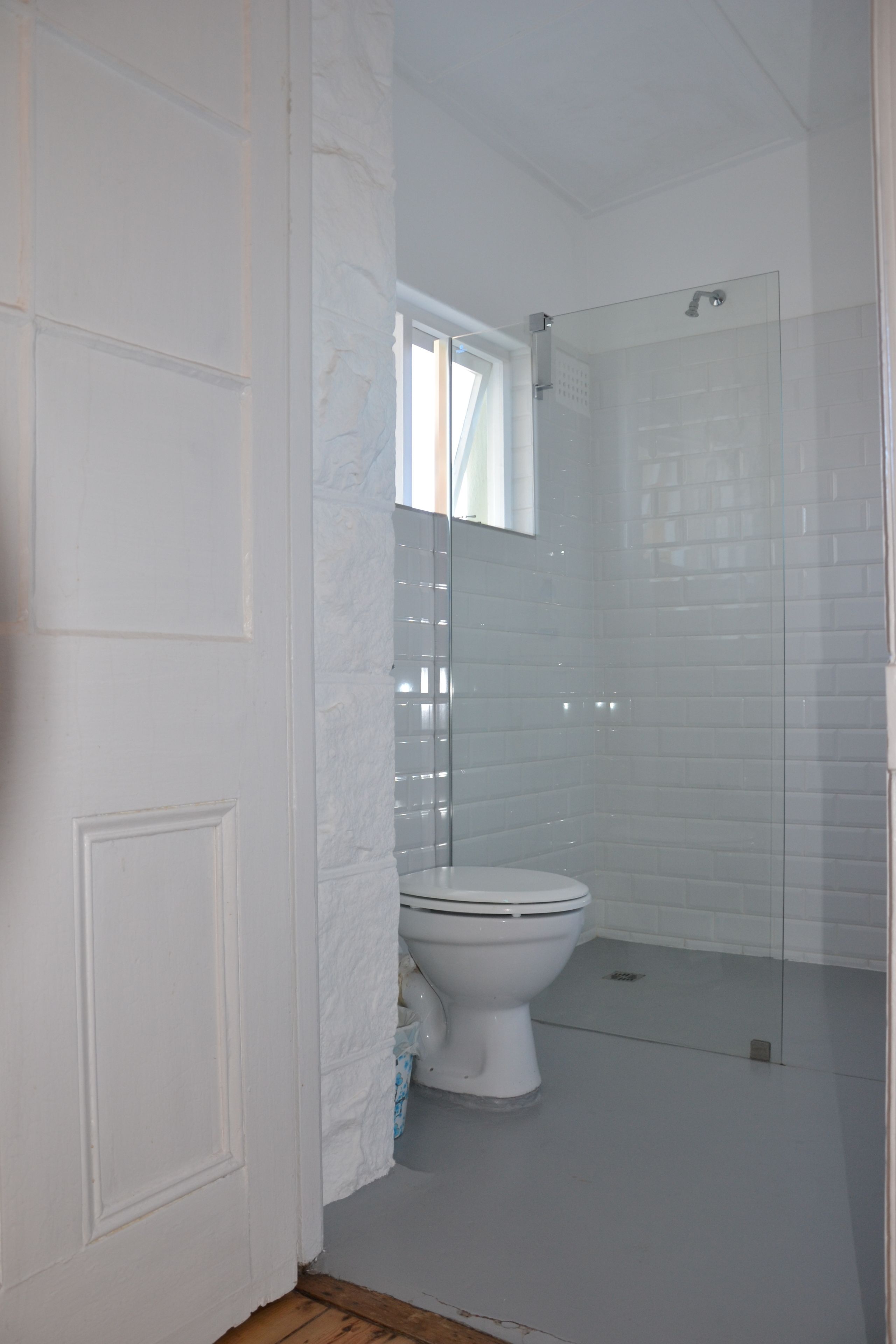 Un baño con inodoro blanco, cabina de ducha de vidrio y paredes con azulejos blancos.