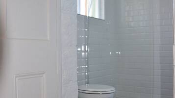 Un baño con inodoro blanco, cabina de ducha de vidrio y paredes con azulejos blancos.