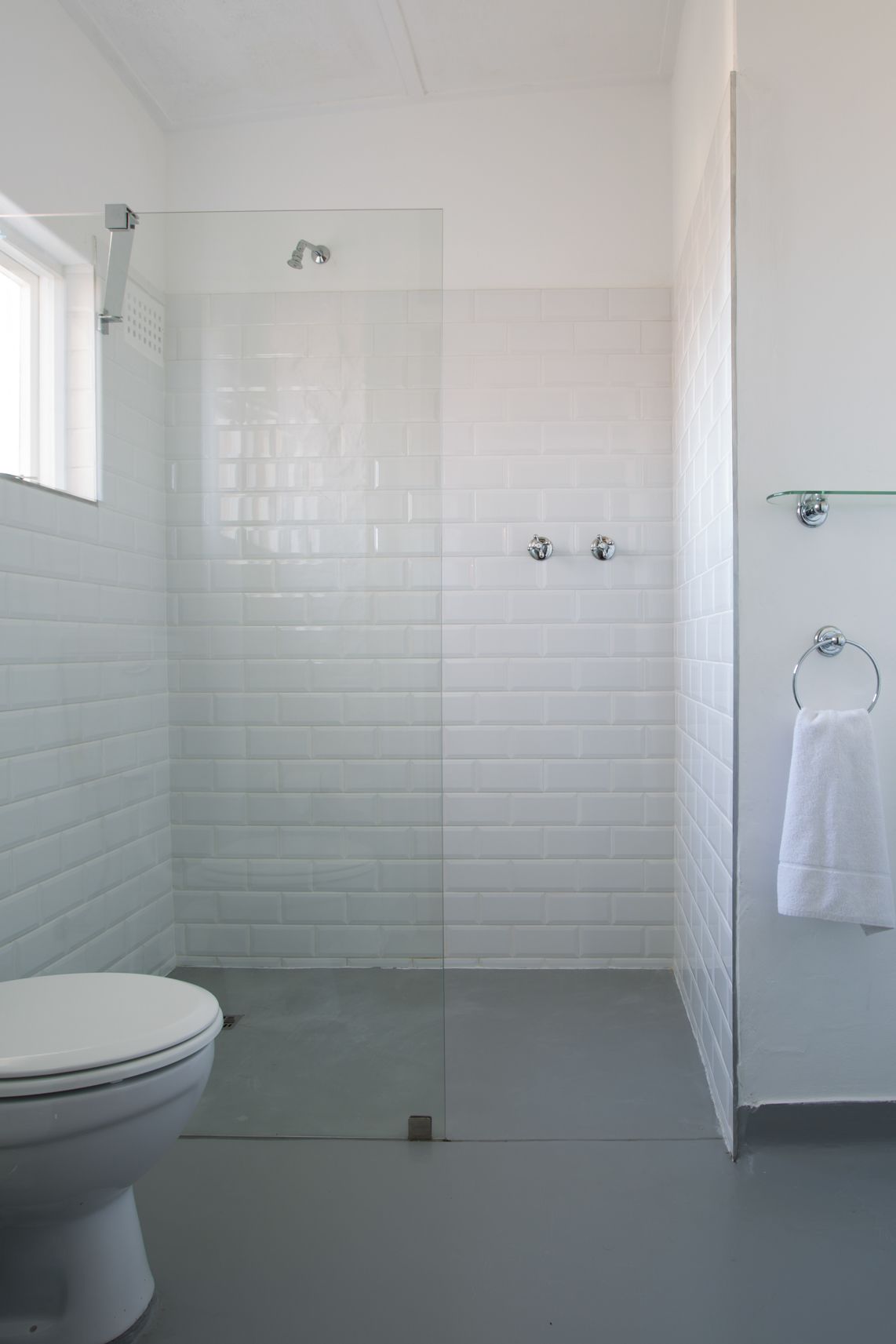 A bathroom with white subway tiles, a toilet, a glass shower enclosure, and a glass shelf with a towel.