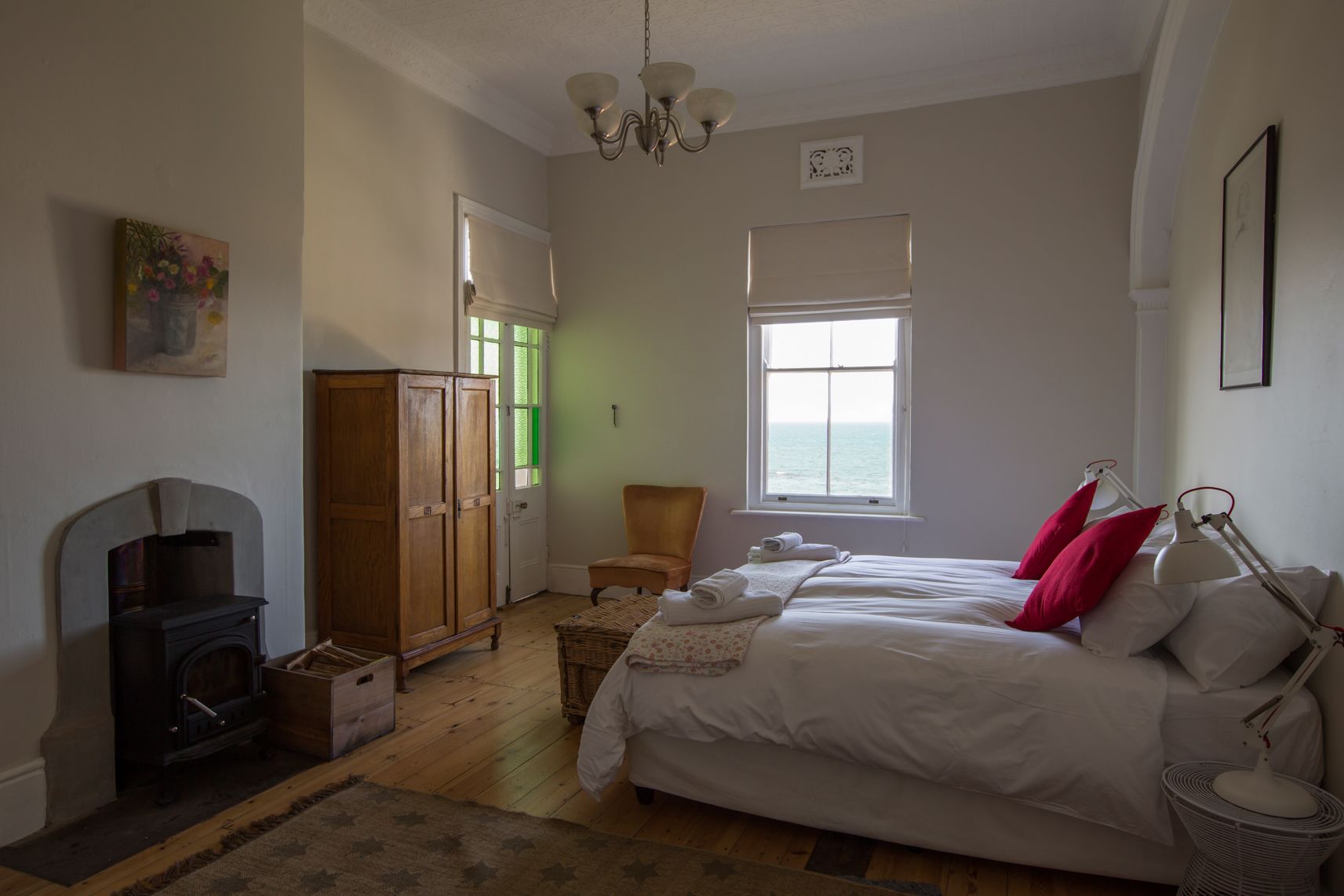 Un dormitorio con cama, una silla, un armario, una chimenea y ventana con vista al mar.