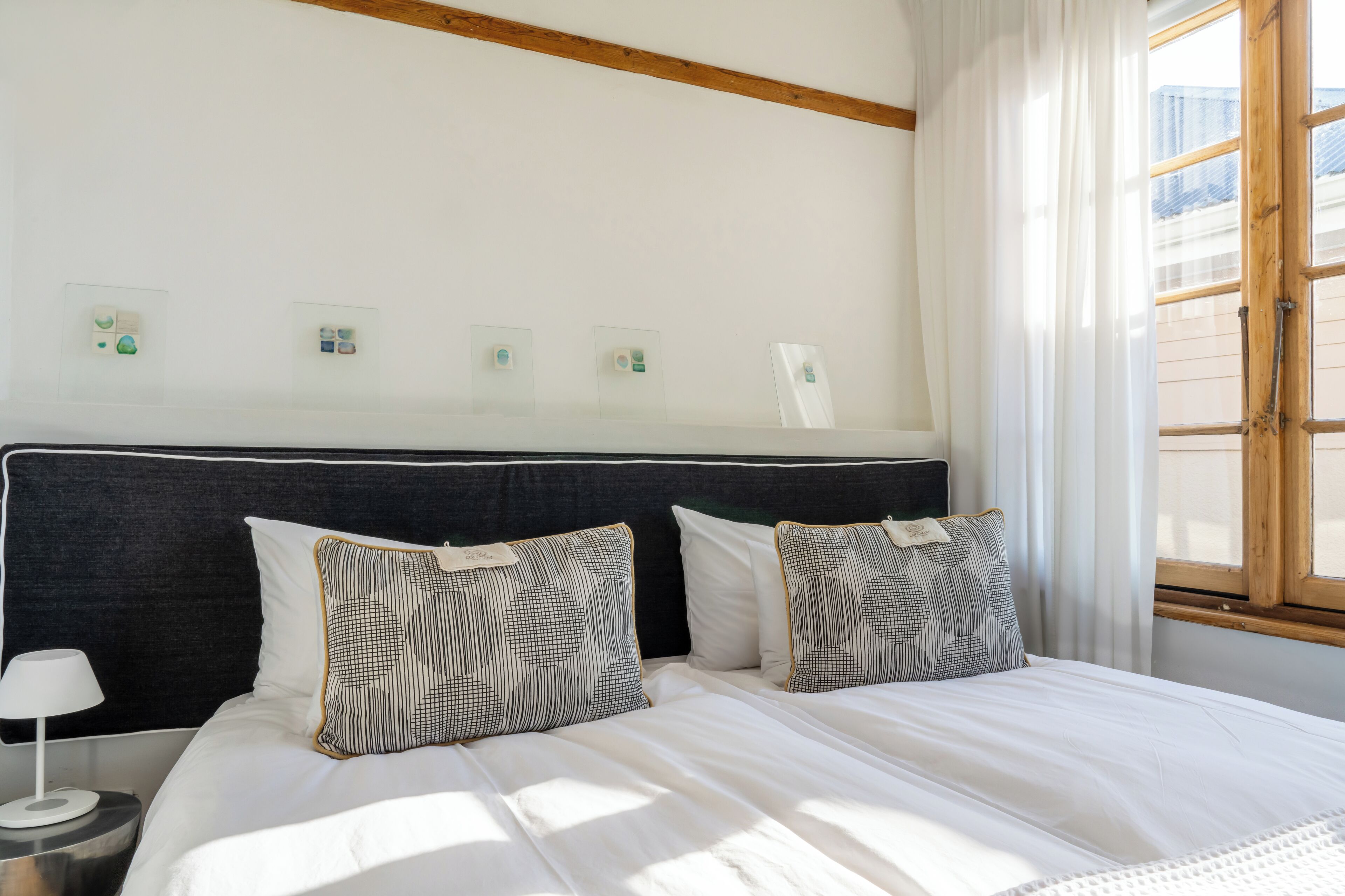 A neatly made bed with patterned pillows, a bedside lamp, and a window with curtains.