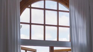 A room with a large window overlooking the sea, a bottle of wine, and a glass on a table.