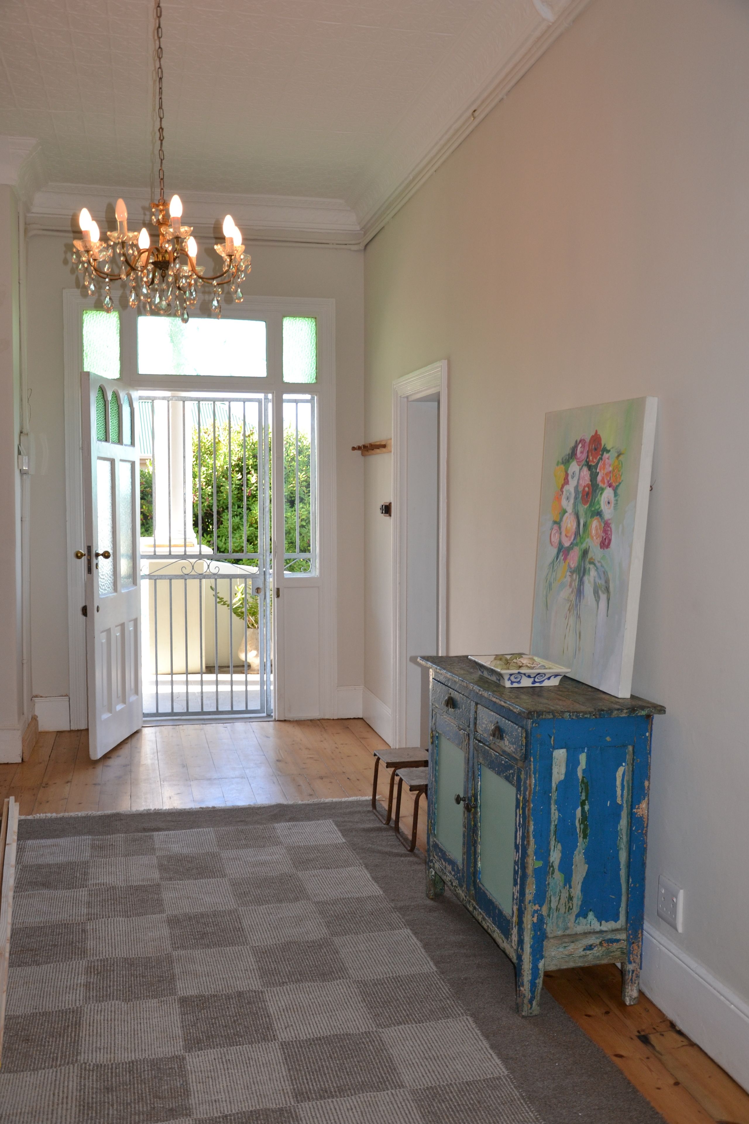 A hallway with a chandelier, a door leading to a balcony, and a painting on the wall.