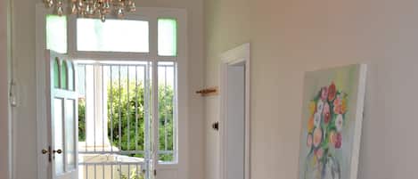 A hallway with a chandelier, a door leading to a balcony, and a painting on the wall.