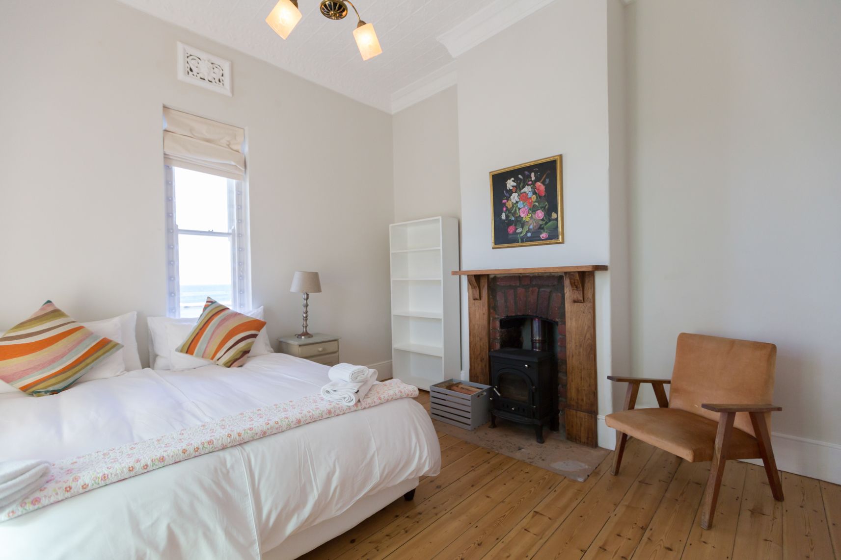 A bedroom with a bed, a chair, a fireplace, and a window.