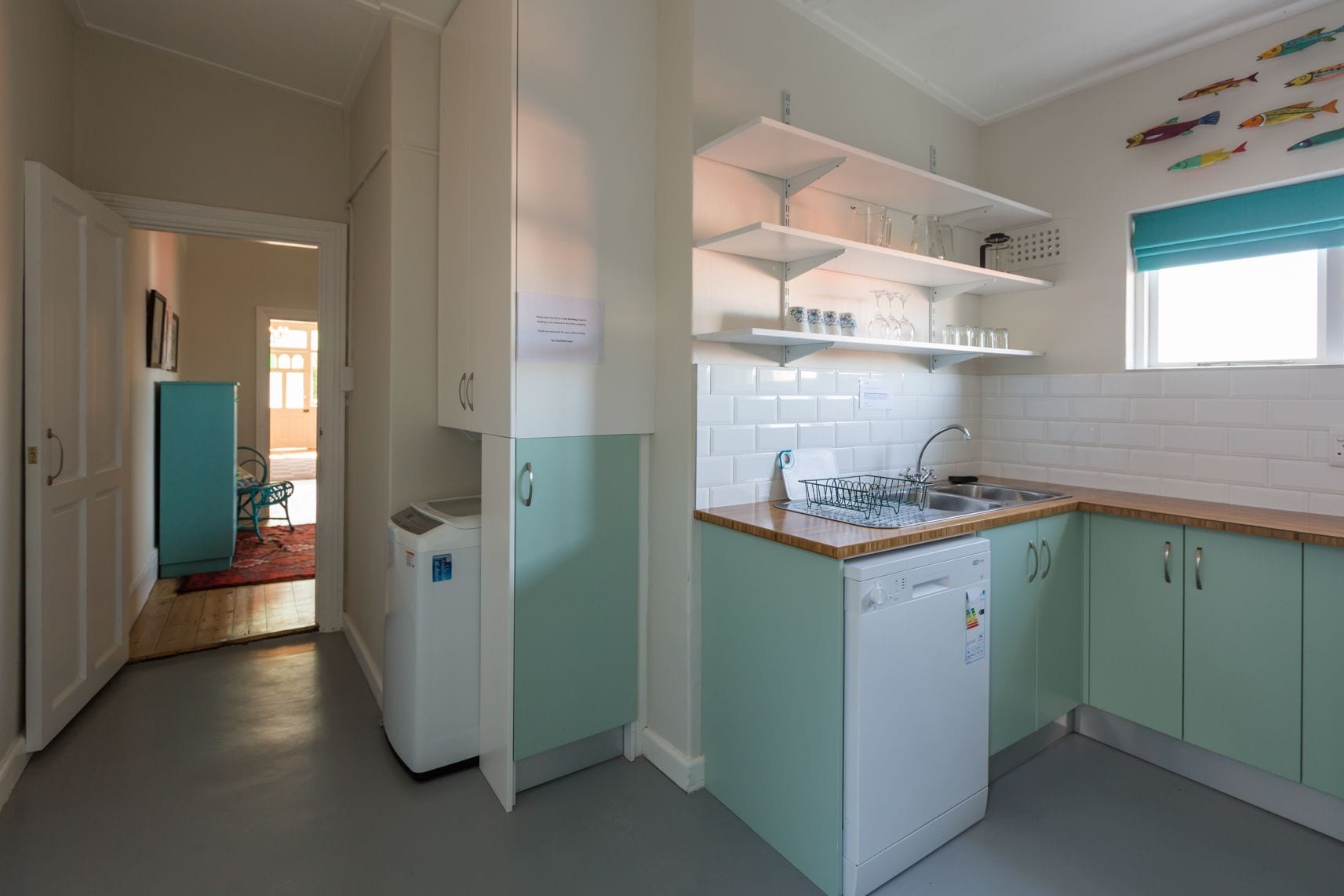 A kitchen with teal cabinets, a dishwasher, and a window with a blue curtain.