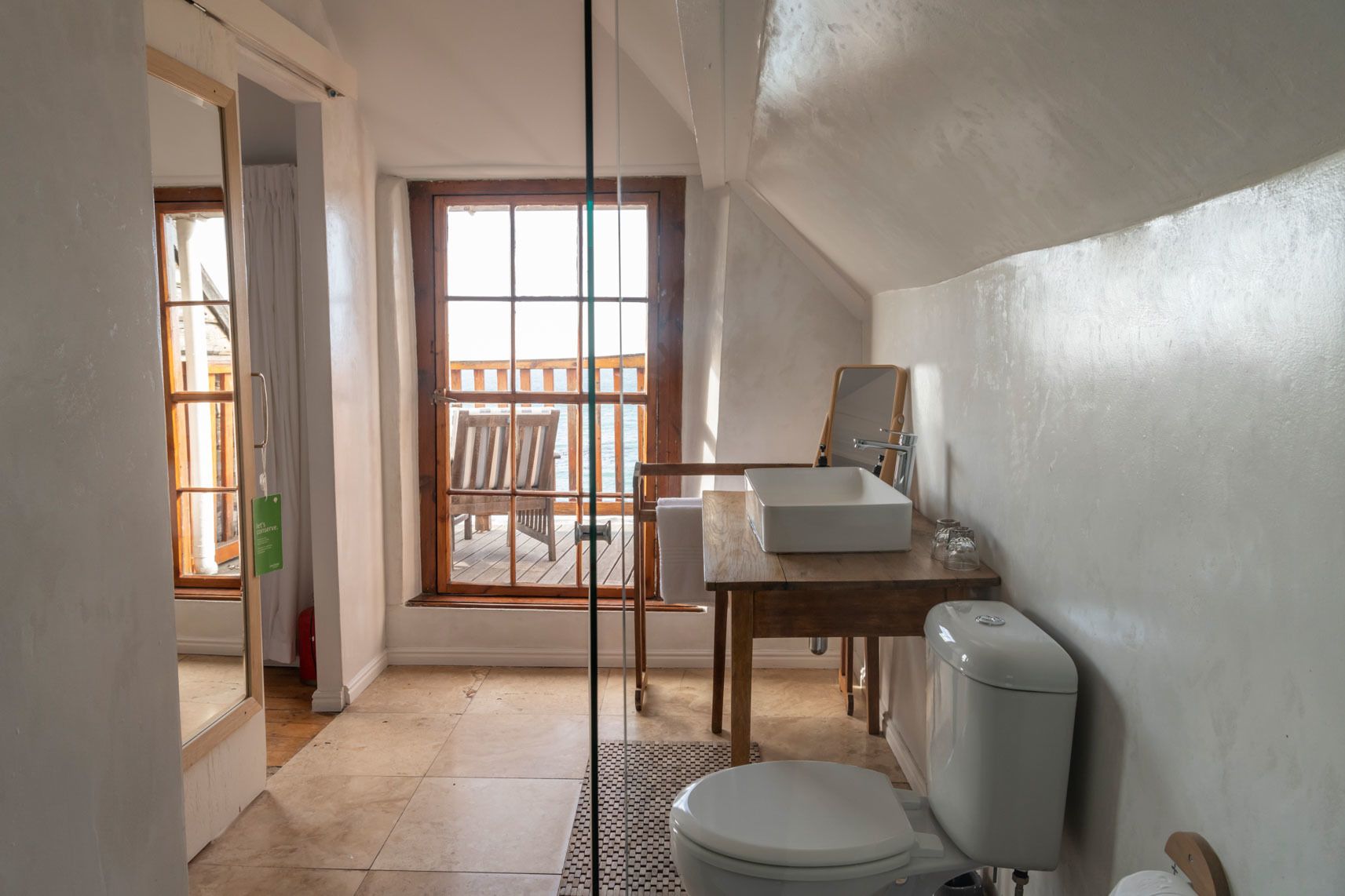 A bathroom with a toilet, sink, and a window overlooking a deck.