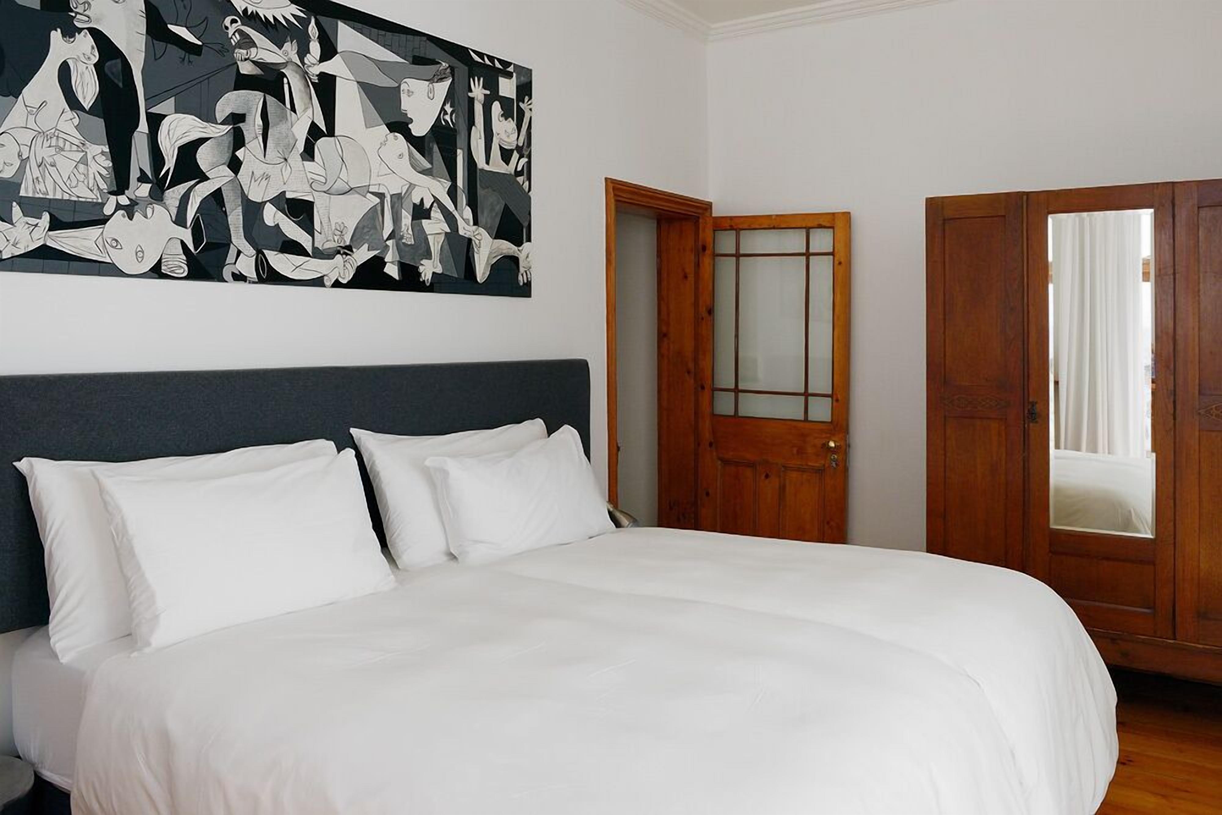 A bedroom with a large bed, a wooden door, and a black and white abstract painting on the wall.