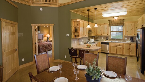 A spacious kitchen with wooden cabinets, a dining area with a table set for four, and a view of the living area. - WorldMark New Braunfels (New Braunfels)