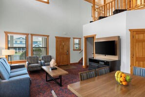 Uma sala de estar espaçosa com teto alto, TV de tela plana na parede e área de jantar com mesa e cadeiras de madeira.