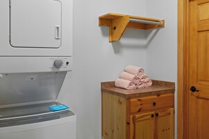 A laundry area with a Whirlpool washer and dryer, a wooden shelf with towels, and a wooden cabinet with a drawer.