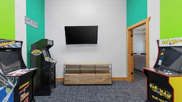 A room with arcade games, a flat-screen TV, and a wooden bench.