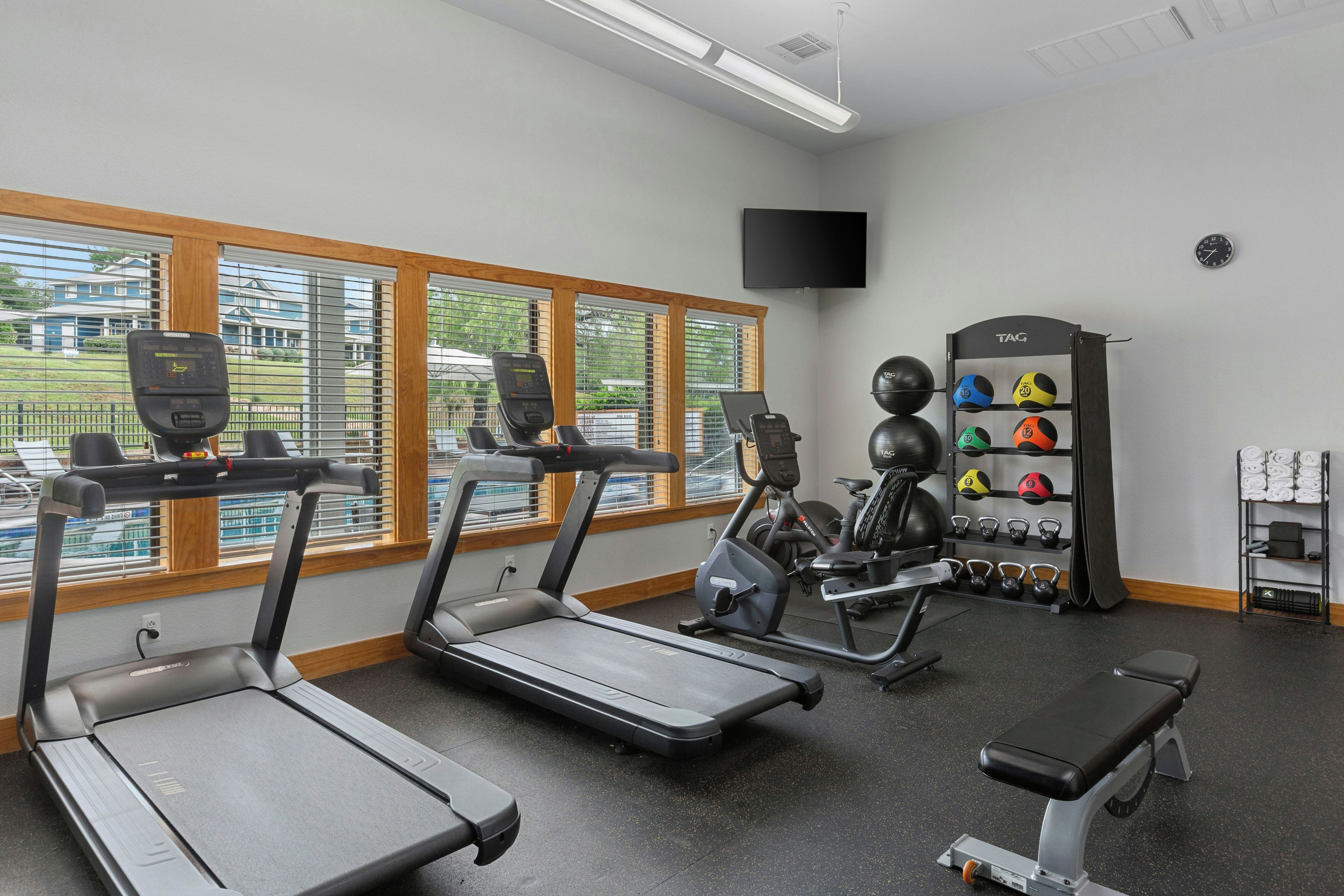 Une salle de sport équipée de tapis de course, d’un appareil elliptique, d’un banc et d’une série de poids et de balles lestées.