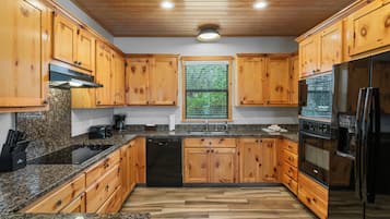 A kitchen with wooden cabinets, granite countertops, a built-in oven, and a window with blinds.