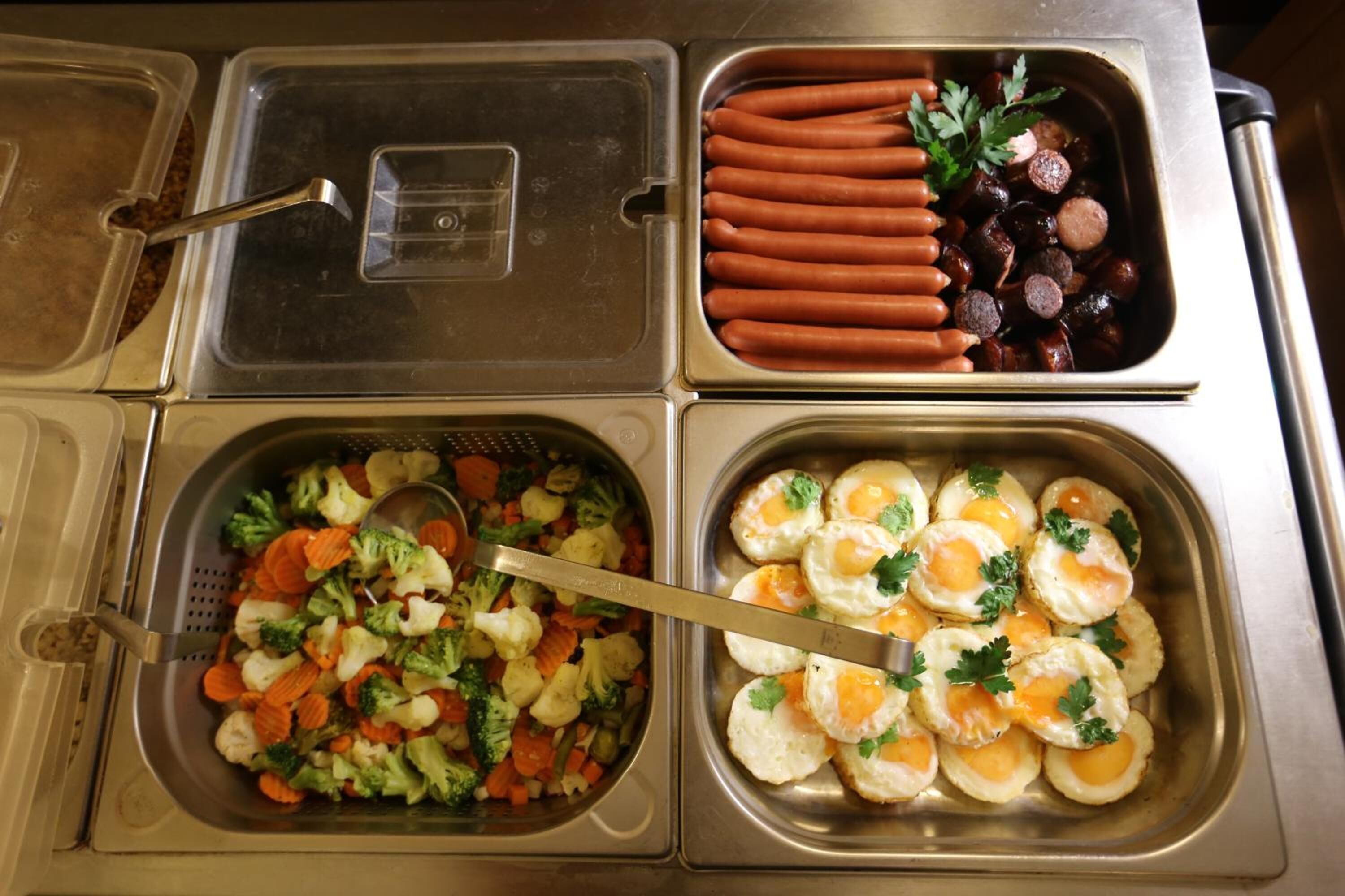 A buffet with various food options including hot dogs, sausages, mixed vegetables, and eggs.