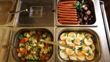 A buffet with various food options including hot dogs, sausages, mixed vegetables, and eggs.