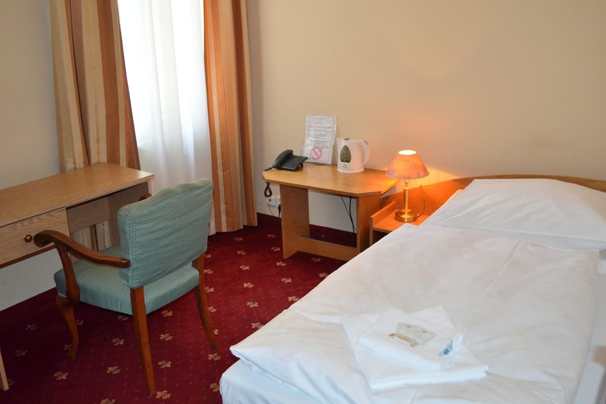 A hotel room with a bed, a desk, a chair, a lamp, a telephone, and a kettle.