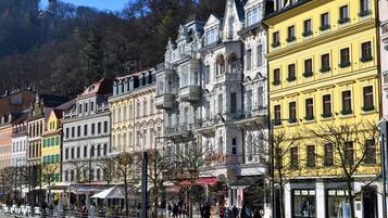 Eine Reihe historischer Gebäude mit verzierten Fassaden und Balkonen, ein Fußweg und ein Fluss im Hintergrund.