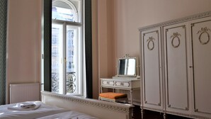 Une chambre d’hôtel avec un lit, une fenêtre donnant sur des immeubles, une commode avec un miroir et un radiateur.