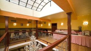Un intérieur à plusieurs niveaux, agrémenté d’un magnifique lustre, de rampes en bois et d’un coin repas avec des nappes roses.