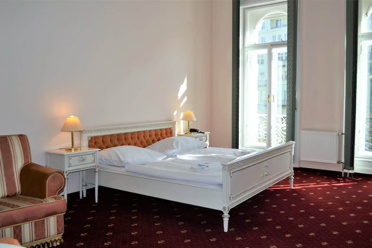 A neatly made bed with white linens, a red upholstered armchair, and two bedside lamps.