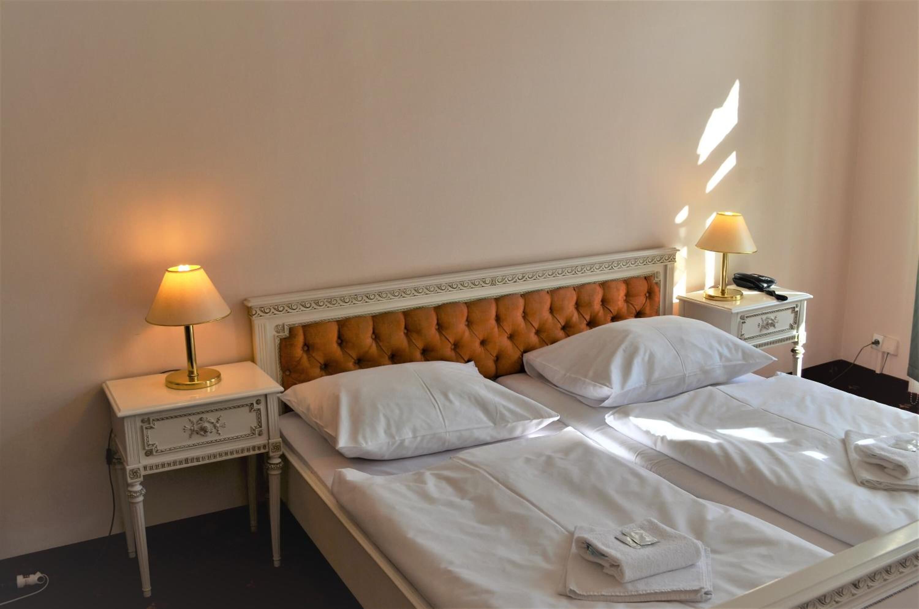 A neatly made bed with white linens, two bedside lamps, and a tufted headboard.