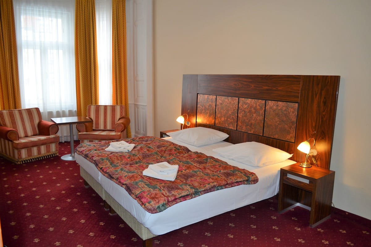 A hotel room with a large bed, two bedside tables with lamps, a striped armchair, and a small table.