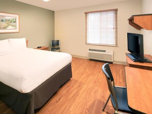 A hotel room with a bed, a desk with a computer, a chair, a TV, and a window with blinds. - Extended Stay America Select Suites - Fayetteville - West (Fayetteville)