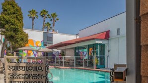 Zona junto a la piscina con piscina, sillas de descanso y un edificio al fondo con murales de colores.