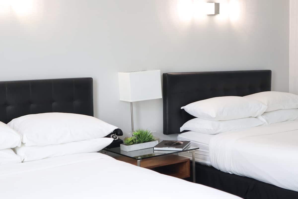 A hotel room with two beds, white bedding, a bedside table with a lamp, a small plant, and a book.