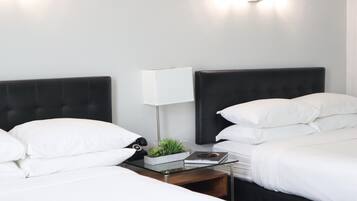 A hotel room with two beds, white bedding, a bedside table with a lamp, a small plant, and a book.